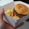 hand holding a burger and chips in a white box