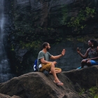 man and woman talking and sitting on a rock near a waterfall