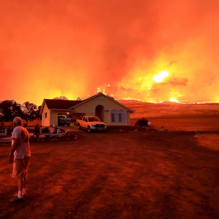 Man looks back at his house while wildfire burns in the distance