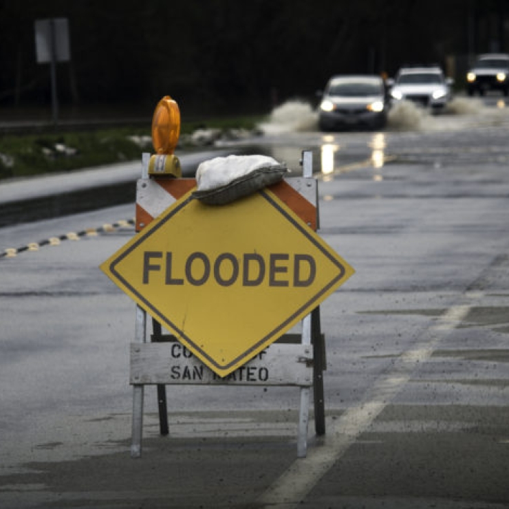 a yellow diamond shaped sign reads "FLOODED" on a wet street