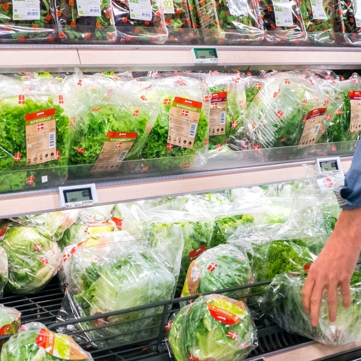 a hand reaches for packaged lettuce on grocery store refrigerated shelves