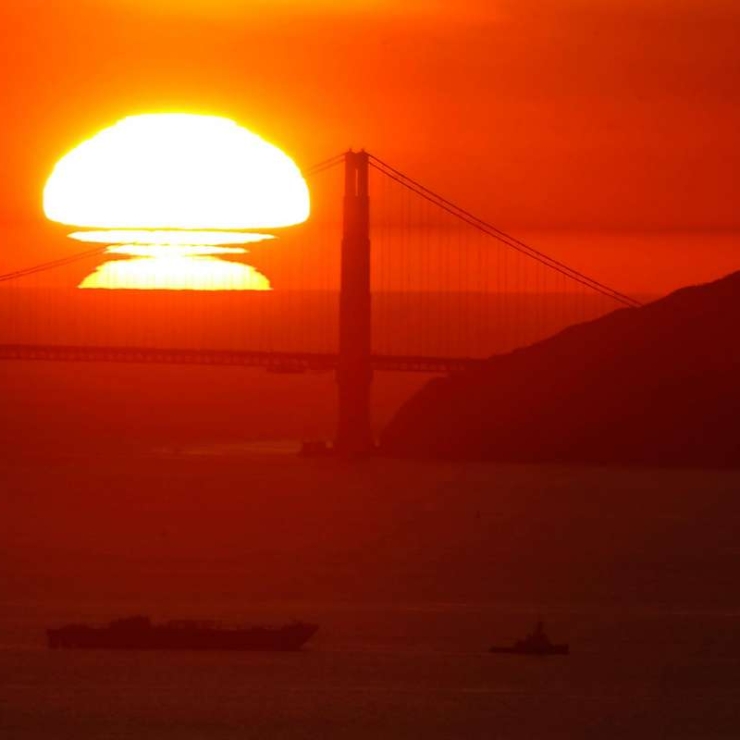 a large orange sun sets behind the Golden Gate Bridge