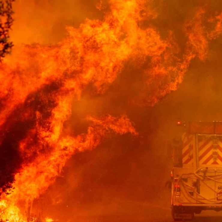 A fire truck drives next to large flames